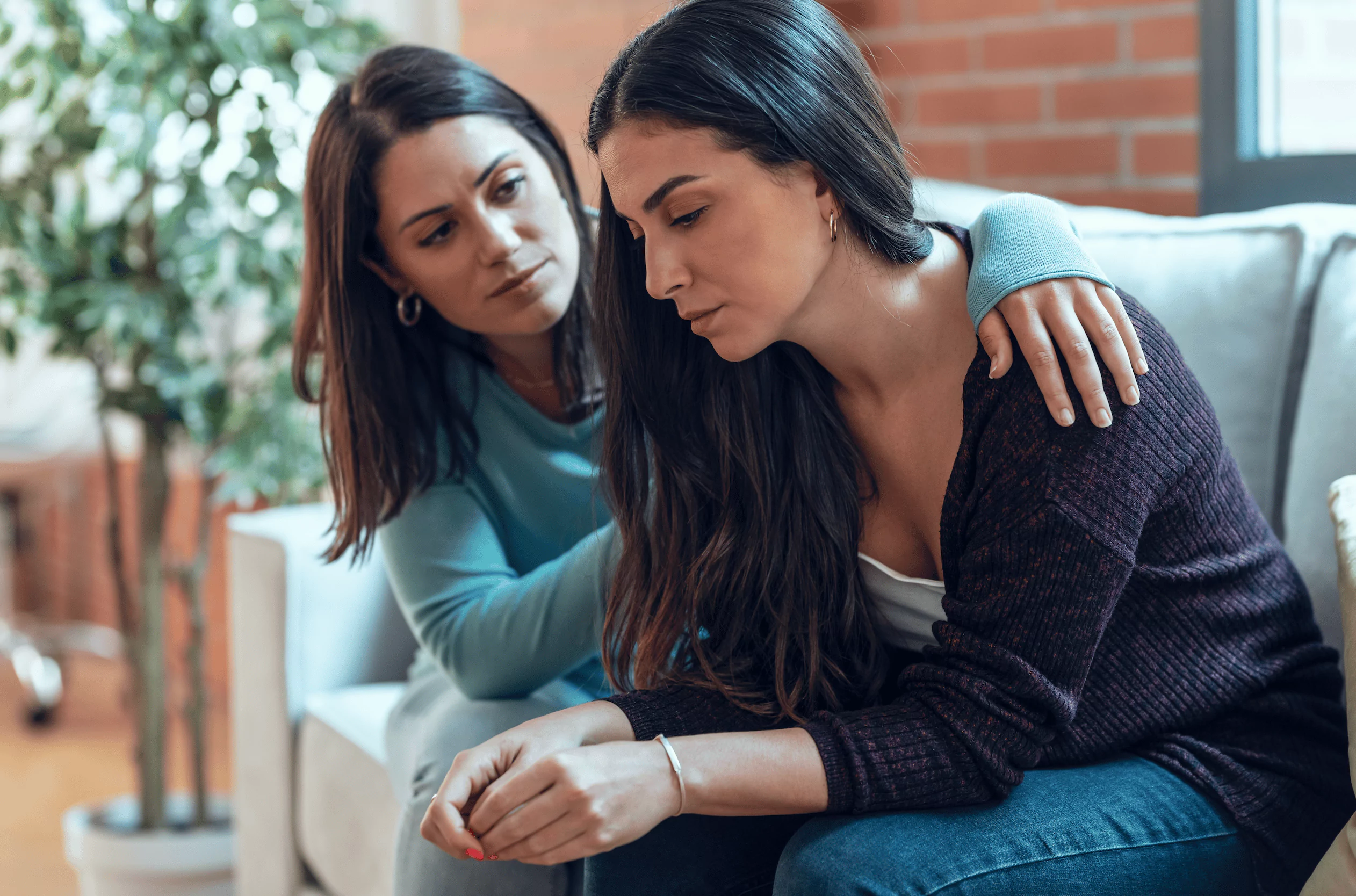 A woman comforting her friend on a couch who is sad